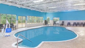 An indoor swimming pool with a blue interior, large windows, and a tiled floor.
