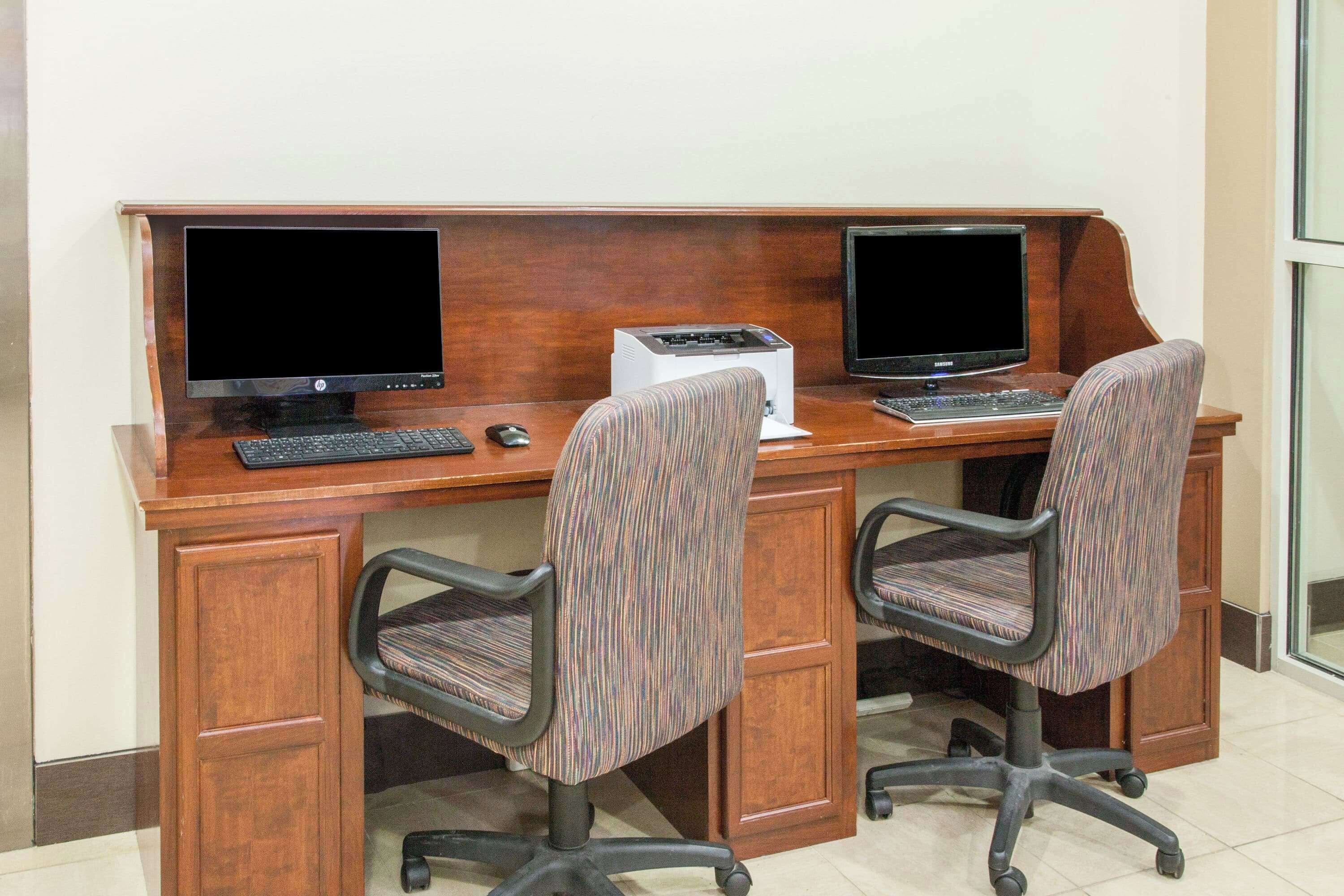 A wooden desk with two monitors, a keyboard, and two office chairs.