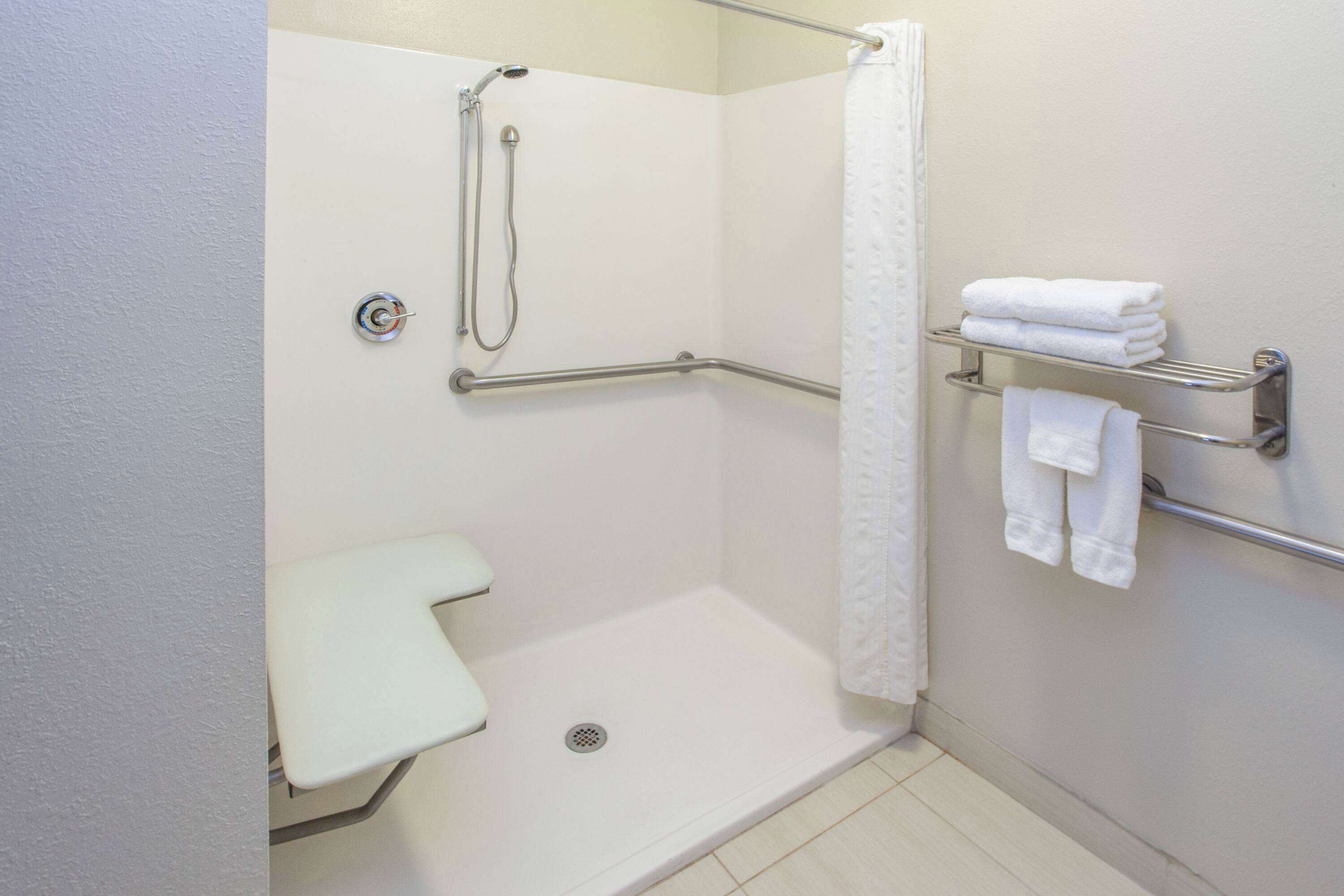 A wheelchair-accessible shower with grab bars, a white toilet, and a towel rack with folded towels.