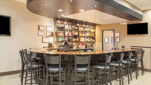 A bar area with a round table and multiple bar stools, a well-stocked liquor shelf, and a flat-screen TV mounted on the wall.