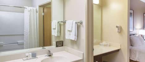 Un baño de hotel con lavamanos, espejo, toallero y un pequeño banco.