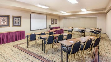 A conference room with a carpeted floor, tables, chairs, a projector screen, and framed pictures on the walls.