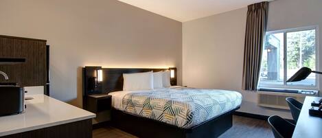 Una habitación de hotel moderna con cama, mesita de noche, lámpara, escritorio, silla y ventana con cortinas.