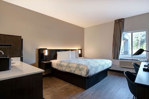 A modern hotel room with a bed, bedside table, lamp, desk, chair, and a window with curtains.