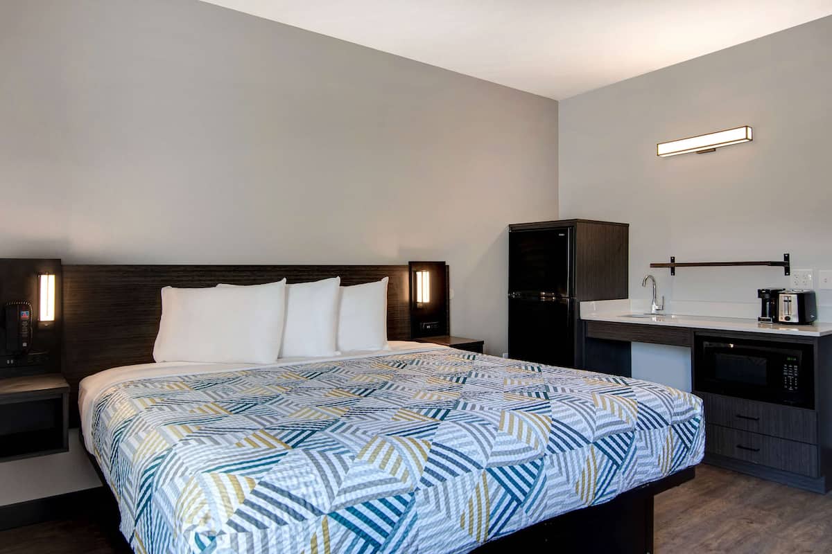 A hotel room with a bed, a nightstand, a desk with a sink, and a microwave.