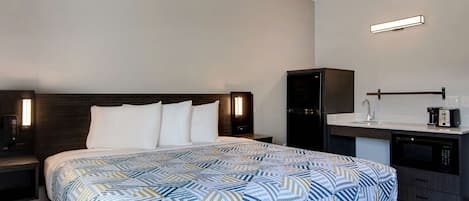 A hotel room with a bed, a nightstand, a desk with a sink, and a microwave.