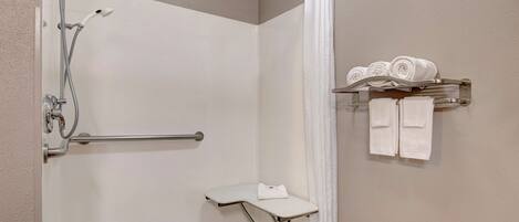 A shower area with a grab bar, a towel rack with towels, and a shower curtain.