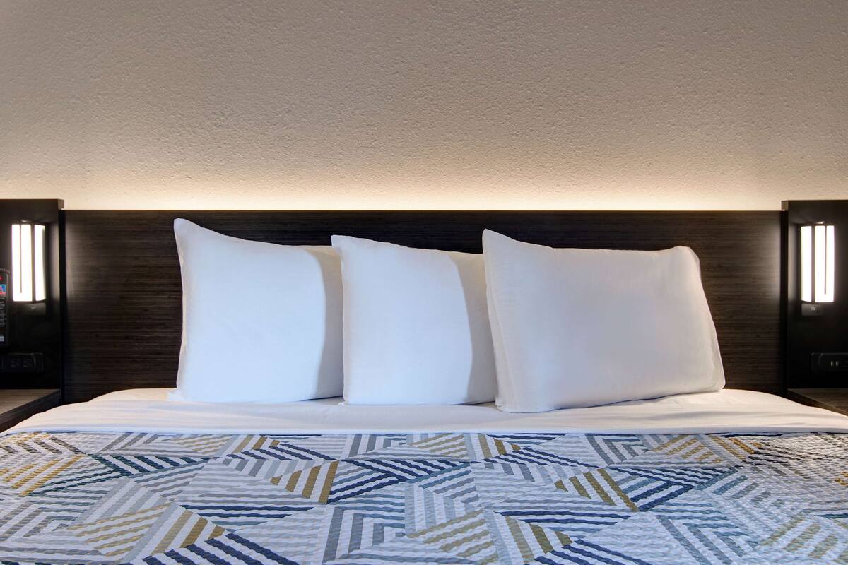 A neatly made bed with a patterned bedspread and three pillows.
