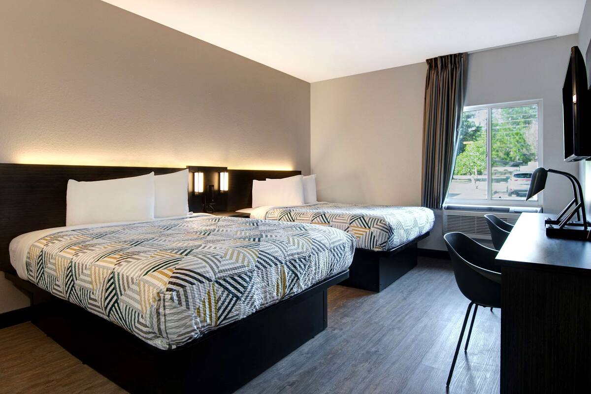 A hotel room with two beds, a desk, and a chair.