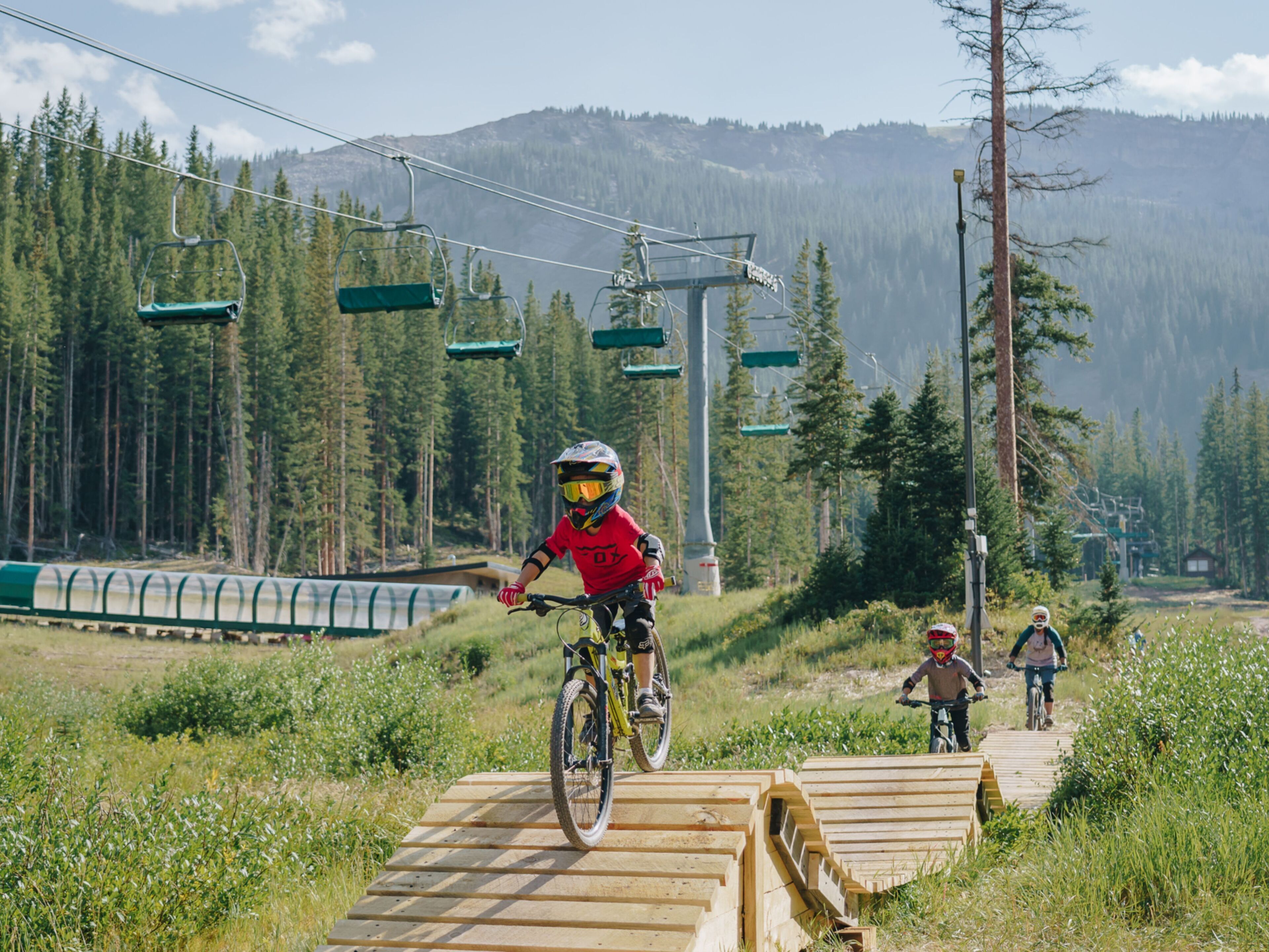 Un sendero de bicicleta de montaña con rampas de madera y un telesilla al fondo.