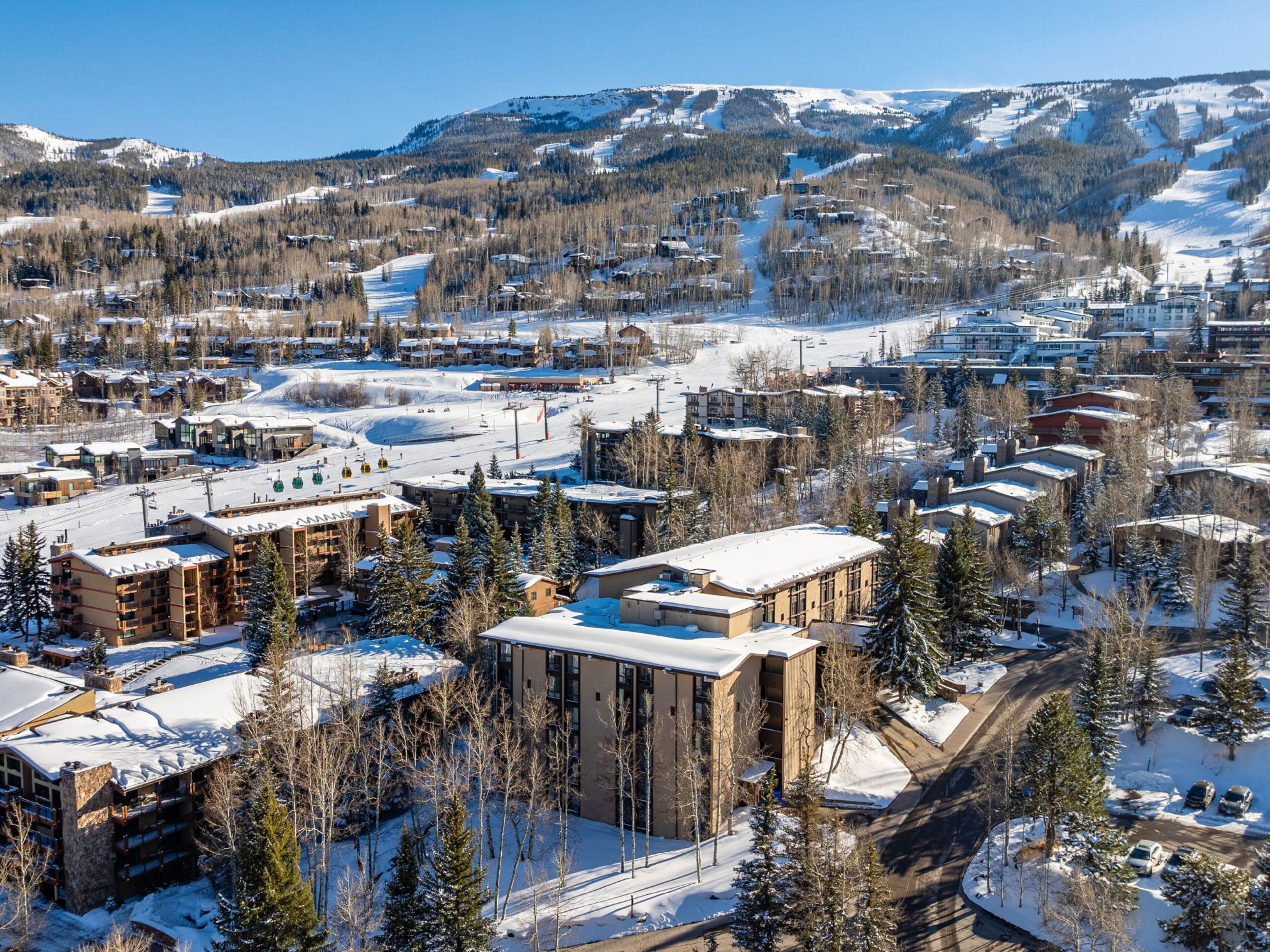 A snow-covered town with modern buildings, a ski lift, and a mountain backdrop.