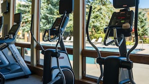 A gym with stationary bikes and treadmills, large windows with a view of trees and a pool. - Stonebridge Inn (Snowmass Village)