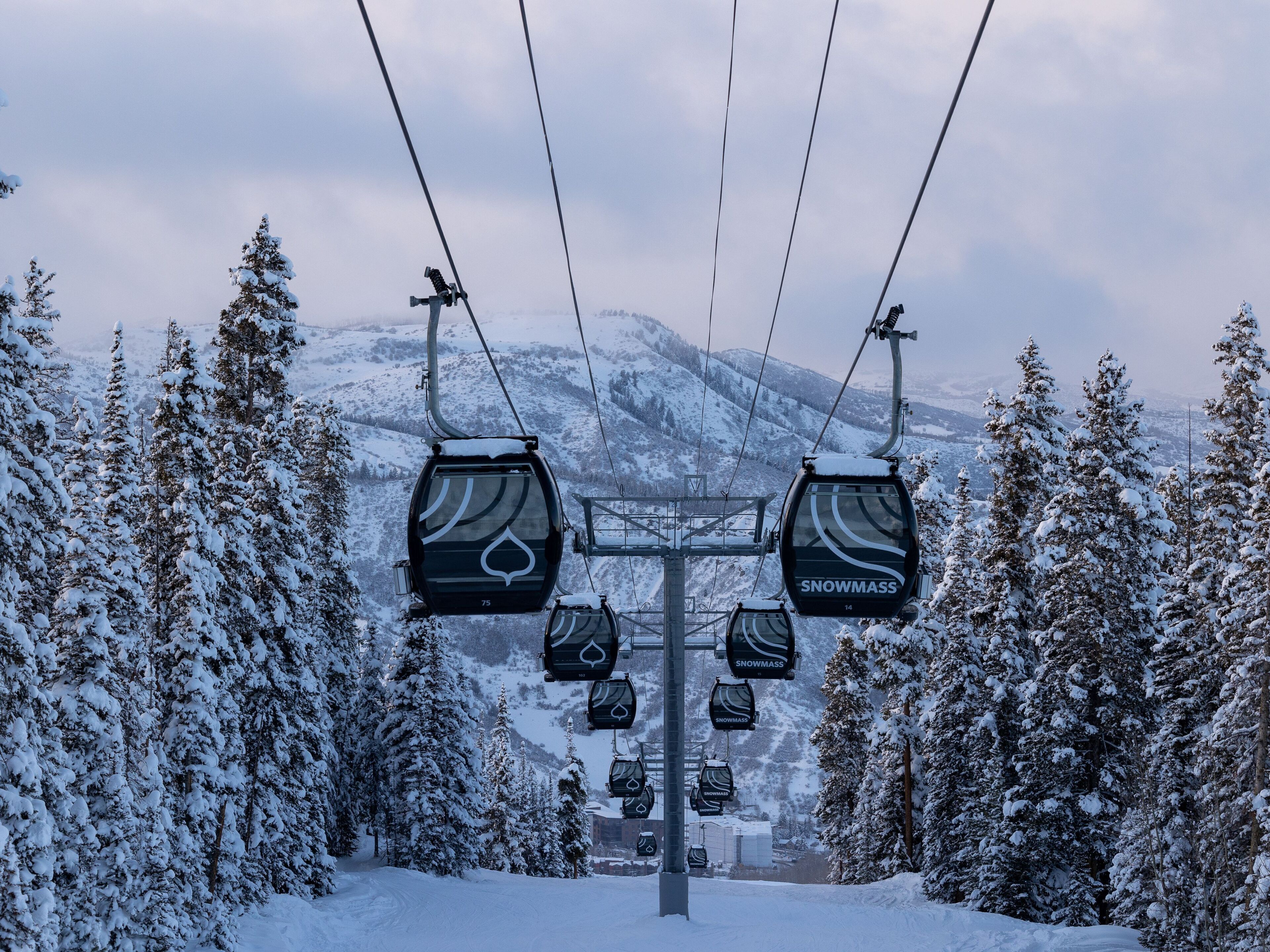 Un télésiège dont les sièges sont marqués du nom « SNOWMASS », avec une montagne enneigée en arrière-plan.