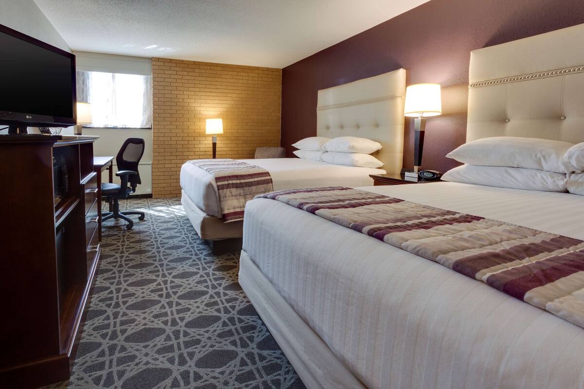 A hotel room with two beds, a TV, a desk, and a chair.
