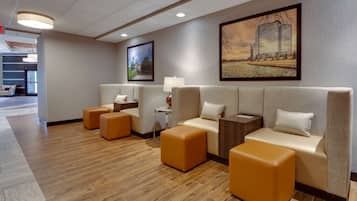 A modern hotel lobby with a sofa set, ottomans, a lamp, and framed artwork on the walls.