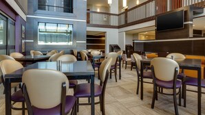 A spacious dining area with multiple tables and chairs, a flat-screen TV mounted on the wall, and a staircase connecting different levels. - Drury Inn & Suites Kansas City Overland Park (Overland Park)