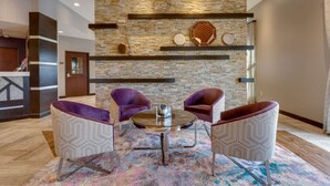 A lobby with a stone wall, two purple armchairs, a glass table, and a patterned rug. - Drury Inn & Suites Kansas City Overland Park (Overland Park)