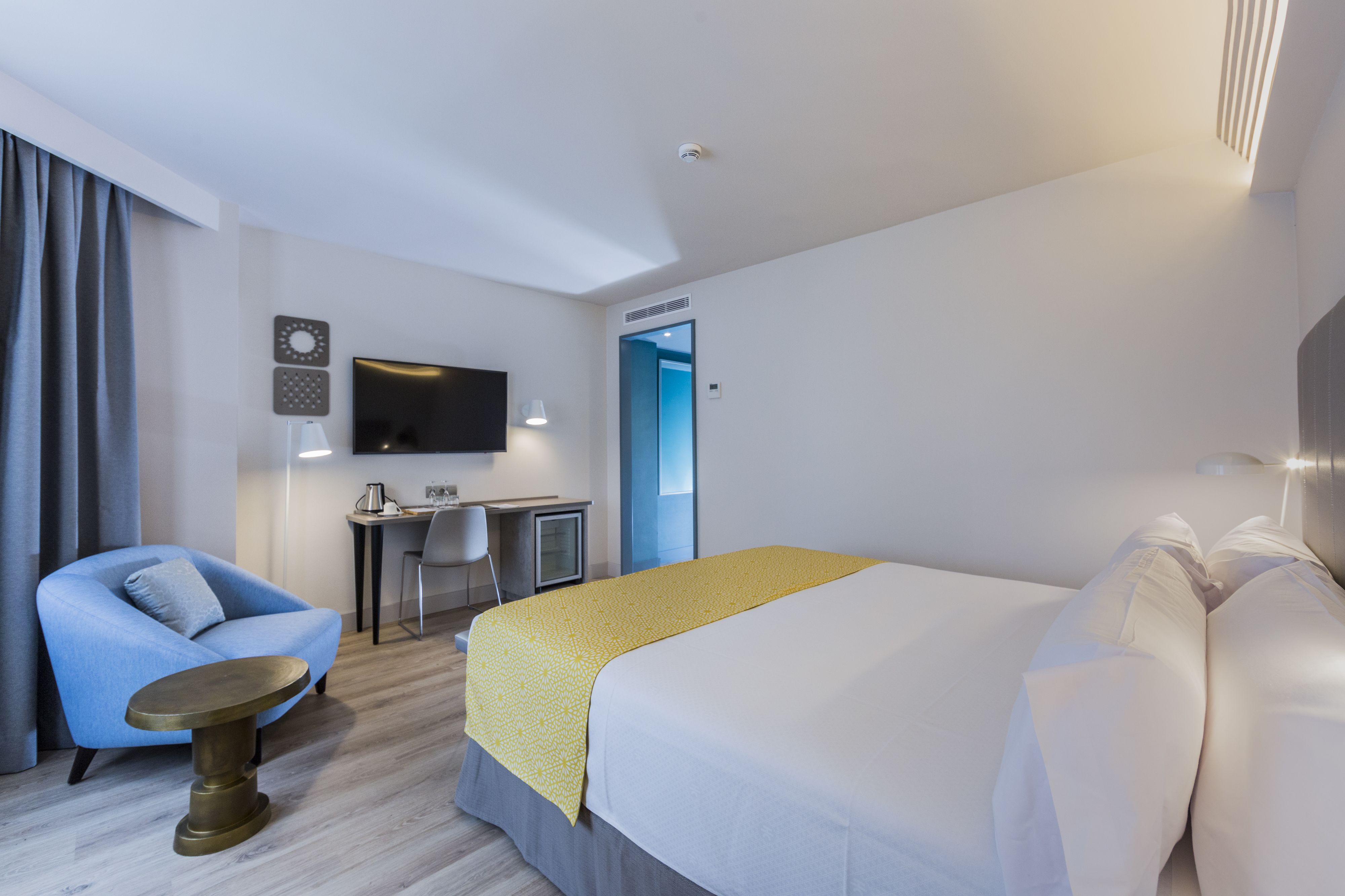Una habitación de hotel moderna con una cama grande, un escritorio con una silla, un televisor y una mesita.