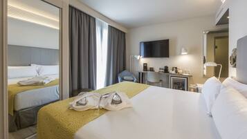 Habitación de hotel con una cama grande, una cama más pequeña, un escritorio con silla, televisión y minibar.