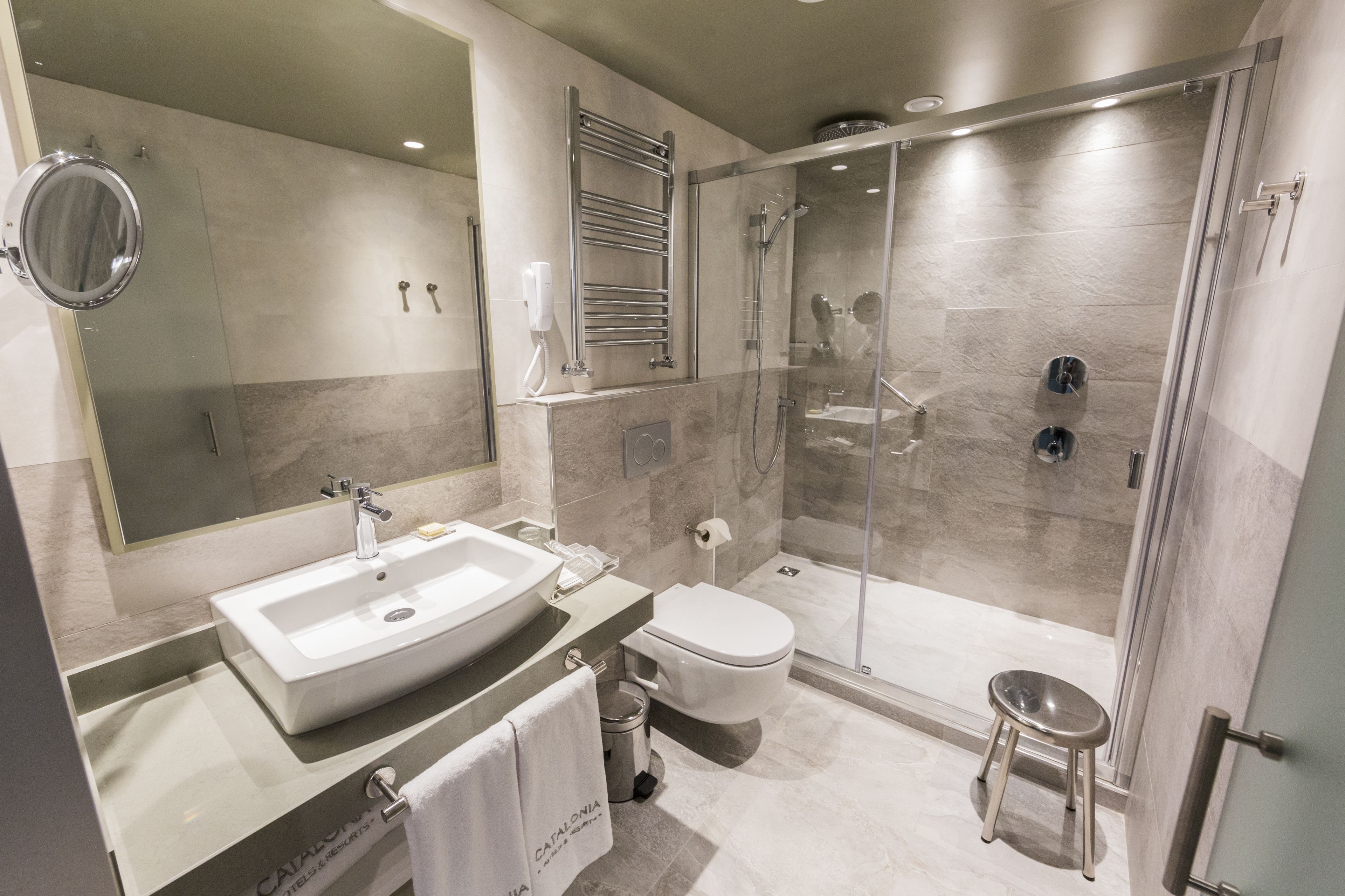 Un baño moderno con un espejo grande, un lavamanos, un inodoro y una zona de ducha con paredes de vidrio.