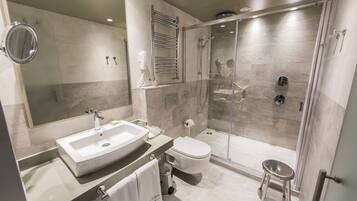 Un baño moderno con un espejo grande, un lavamanos, un inodoro y una zona de ducha con paredes de vidrio.