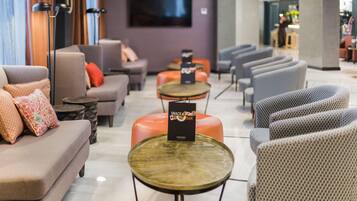 Un área de estar moderna con sofás, sillones y mesas redondas. Un letrero indica una barra de aperitivos.
