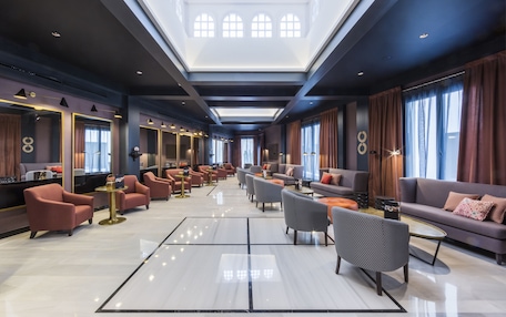 A spacious hotel lobby with multiple seating areas, a central chandelier, and large windows.