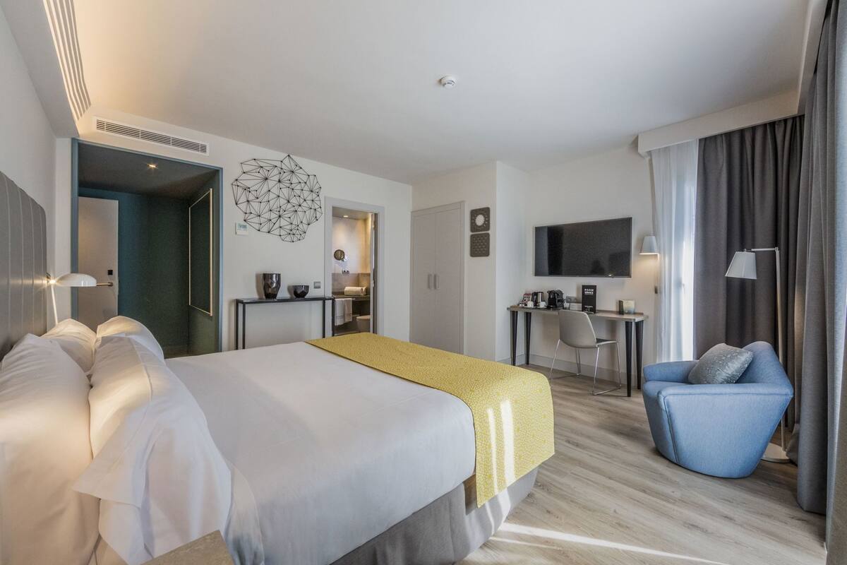 Une chambre d’hôtel avec un lit, un bureau, une chaise, une télévision et une salle de bain visible à travers une porte ouverte.