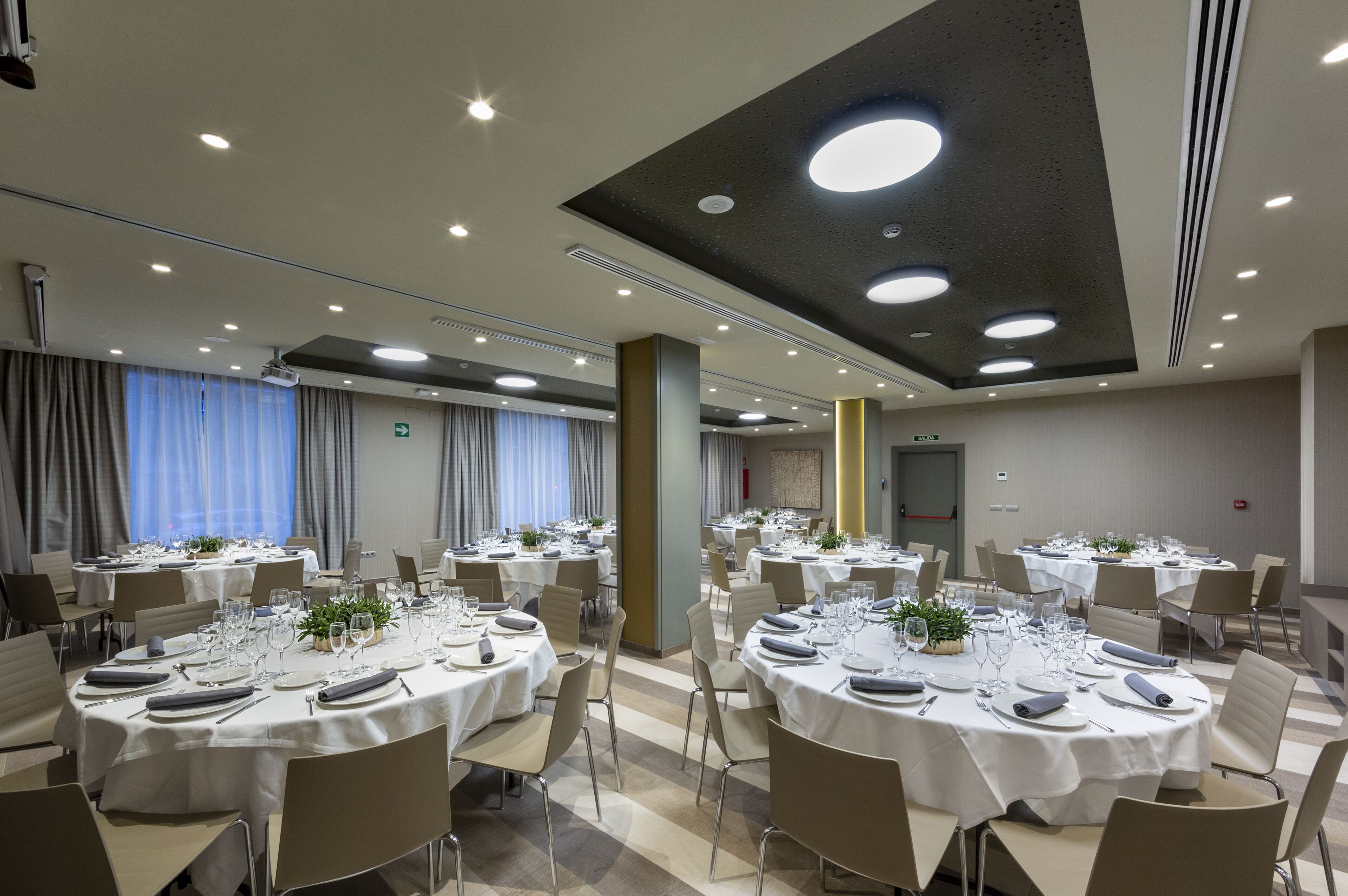 Un salón de conferencias con mesas redondas, sillas e iluminación empotrada en el techo.
