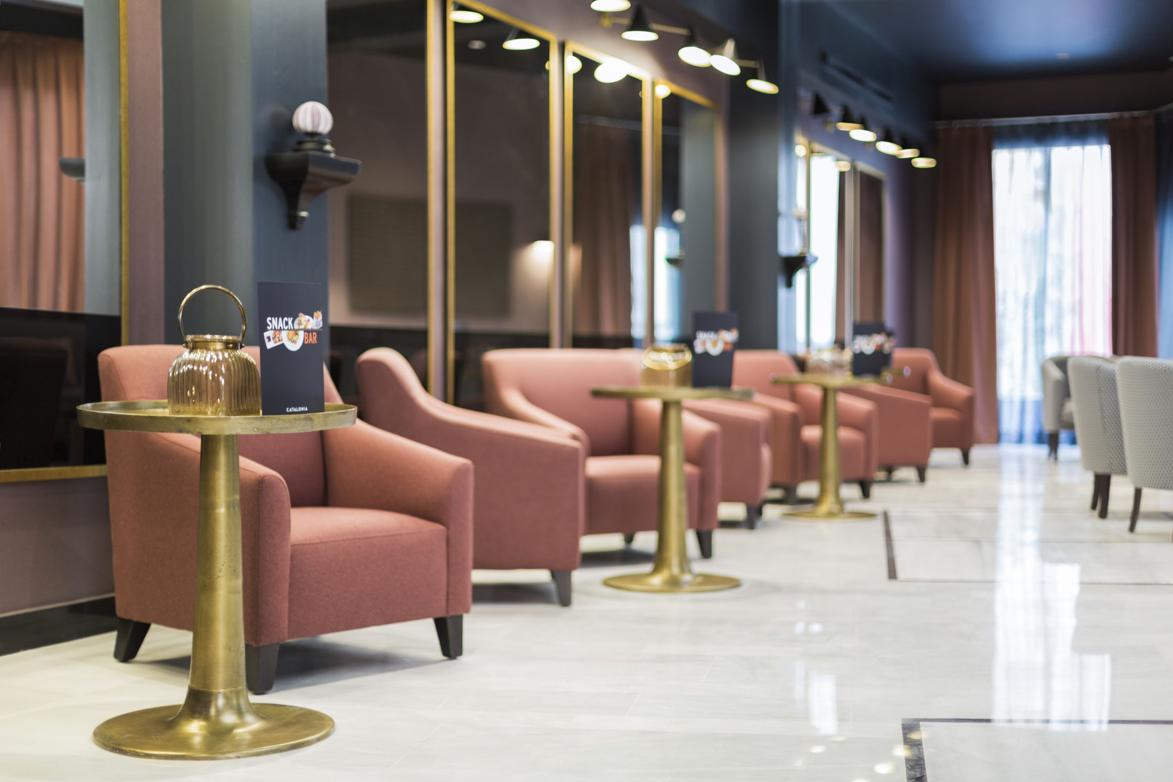 A row of pink armchairs and gold tables in a modern lobby with a marble floor.