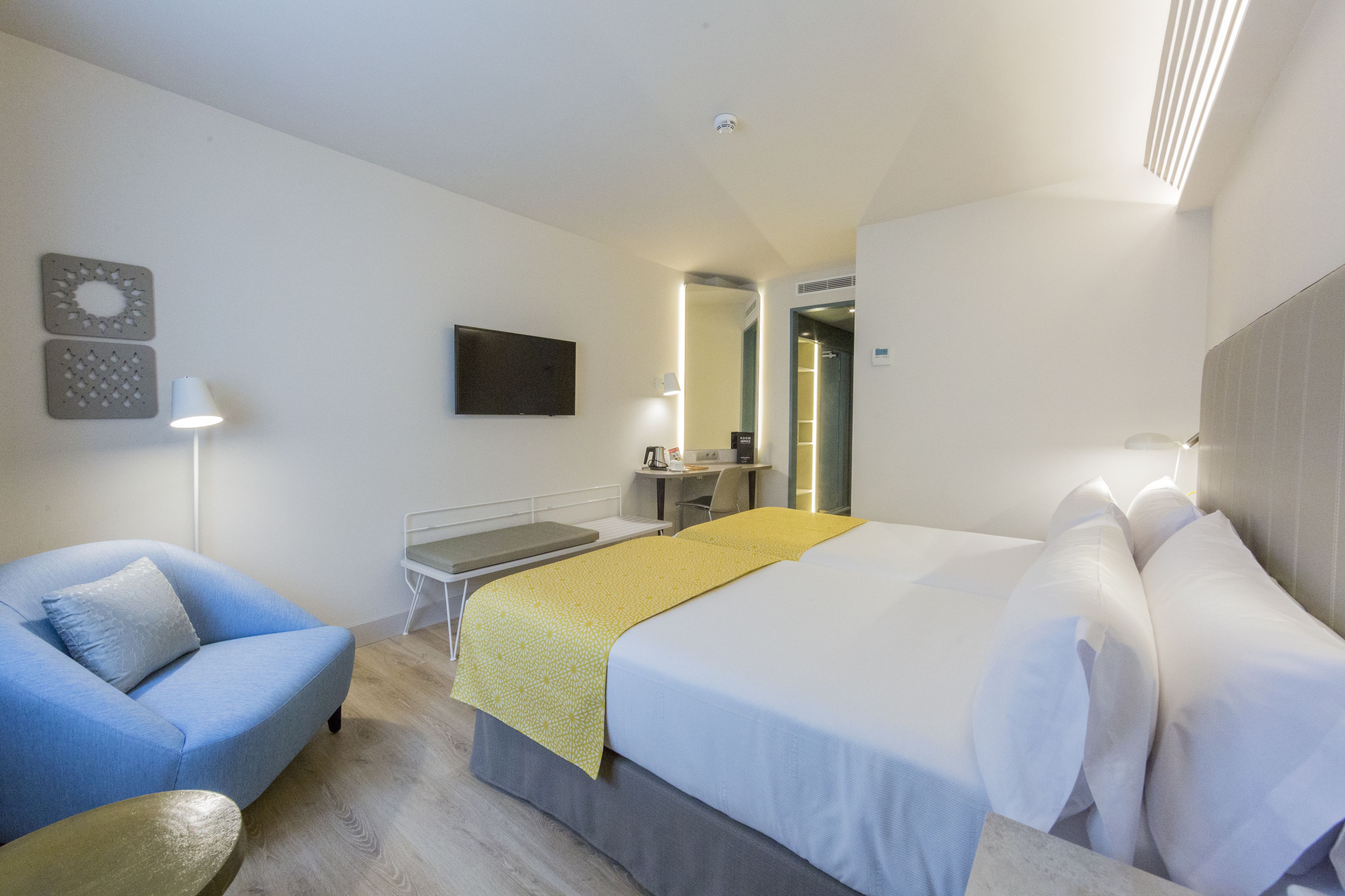 A hotel room with a bed, a desk, a chair, a TV, and a lamp.