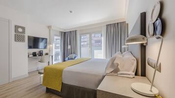 Una habitación de hotel moderna con una cama grande, un escritorio con lámpara, un televisor y vistas a la ciudad a través de amplios ventanales.