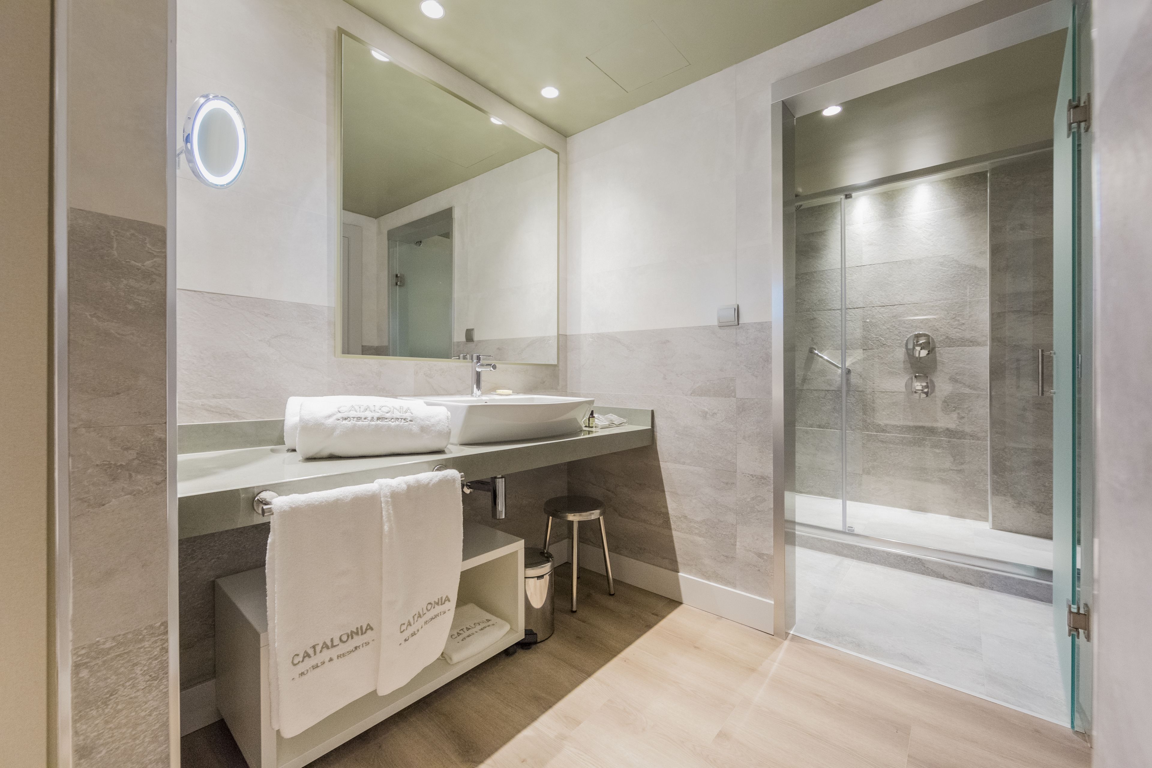 Un baño moderno con un espejo grande, dos lavamanos, una ducha y un tocador con un taburete.