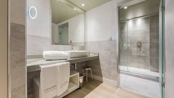Un baño moderno con un espejo grande, dos lavamanos, una ducha y un tocador con un taburete.