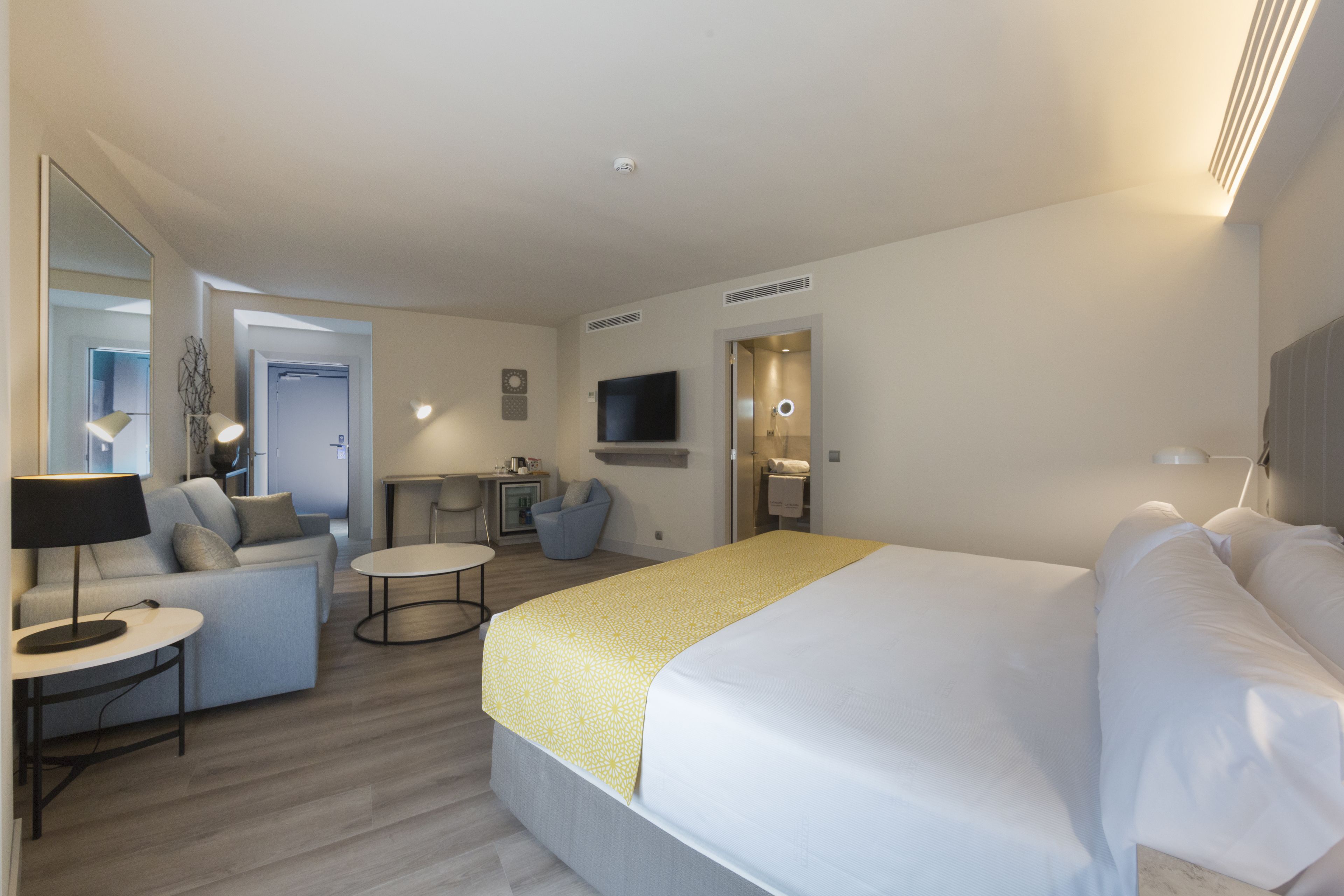 Habitación de hotel moderna con una cama grande, un sofá, una mesita, un televisor y un baño.