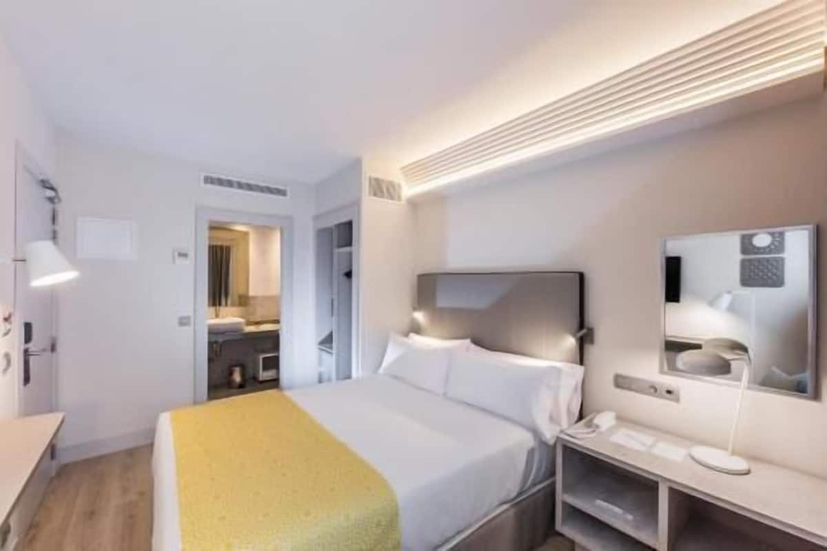 Quarto de hotel com cama, mesa de cabeceira e espelho.