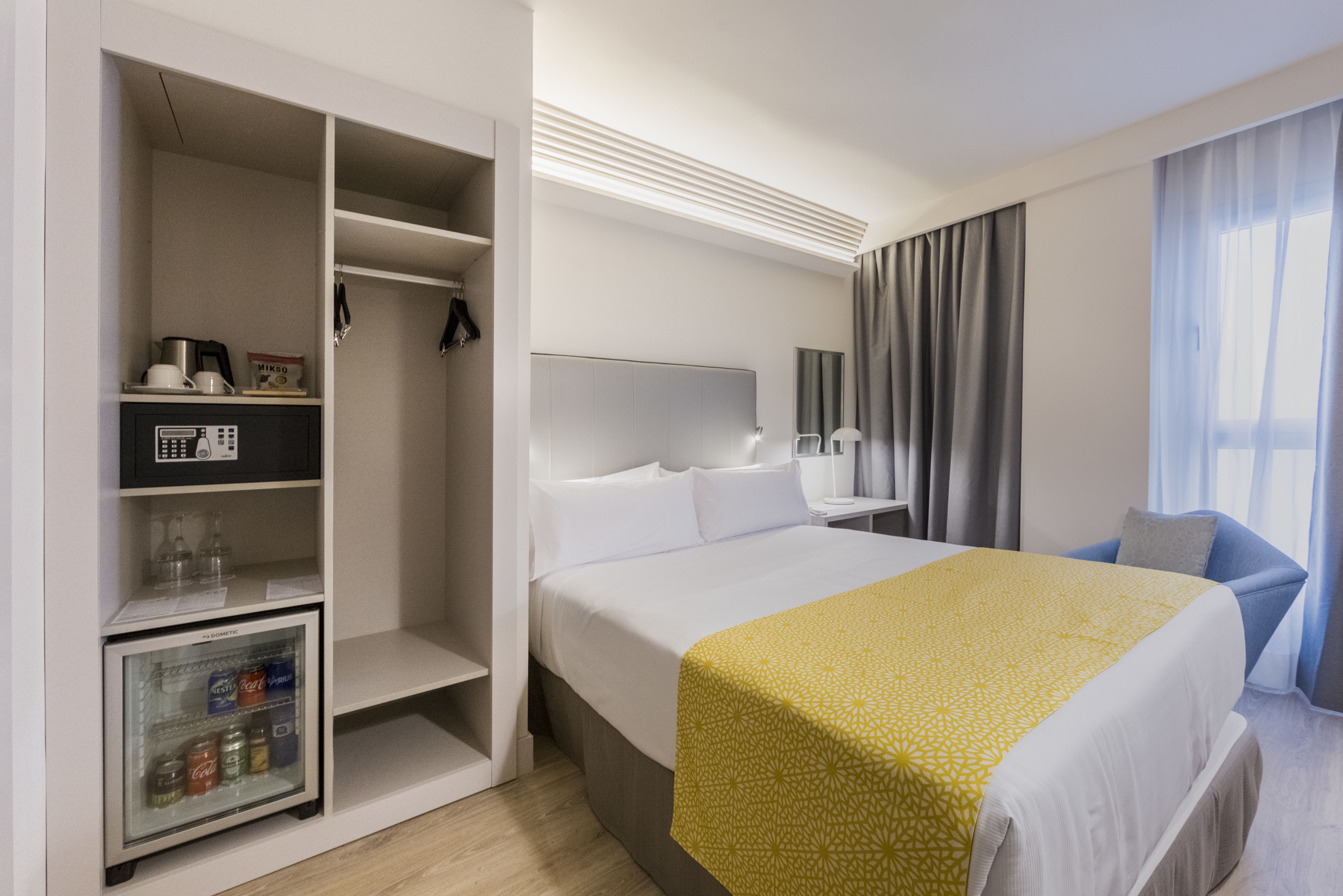 Habitación de hotel con cama, armario, minibar y zona de estar.