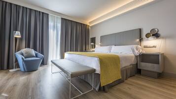 A modern hotel room with a large bed, a bench, a chair, a bedside table, and a nightstand.
