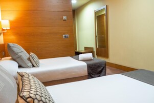 A hotel room with two single beds, a wooden panel wall, a small table, and a mirror.