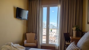 Ett hotellrum med en säng, en stol, en tv och en balkong med utsikt.