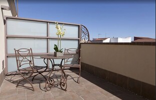Eine Terrasse mit einem Metalltisch und -stühlen, einem Blumentopf und einem dekorativen Metallzaun.