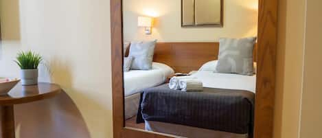 A hotel room with a bed, bedside table, lamp, and a mirror reflecting the room.