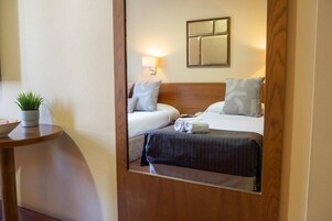 Ein Hotelzimmer mit Bett, Nachttisch, Lampe und einem Spiegel, der den Raum reflektiert.