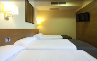 A hotel room with three beds, a wall-mounted TV, and a wall-mounted lamp.