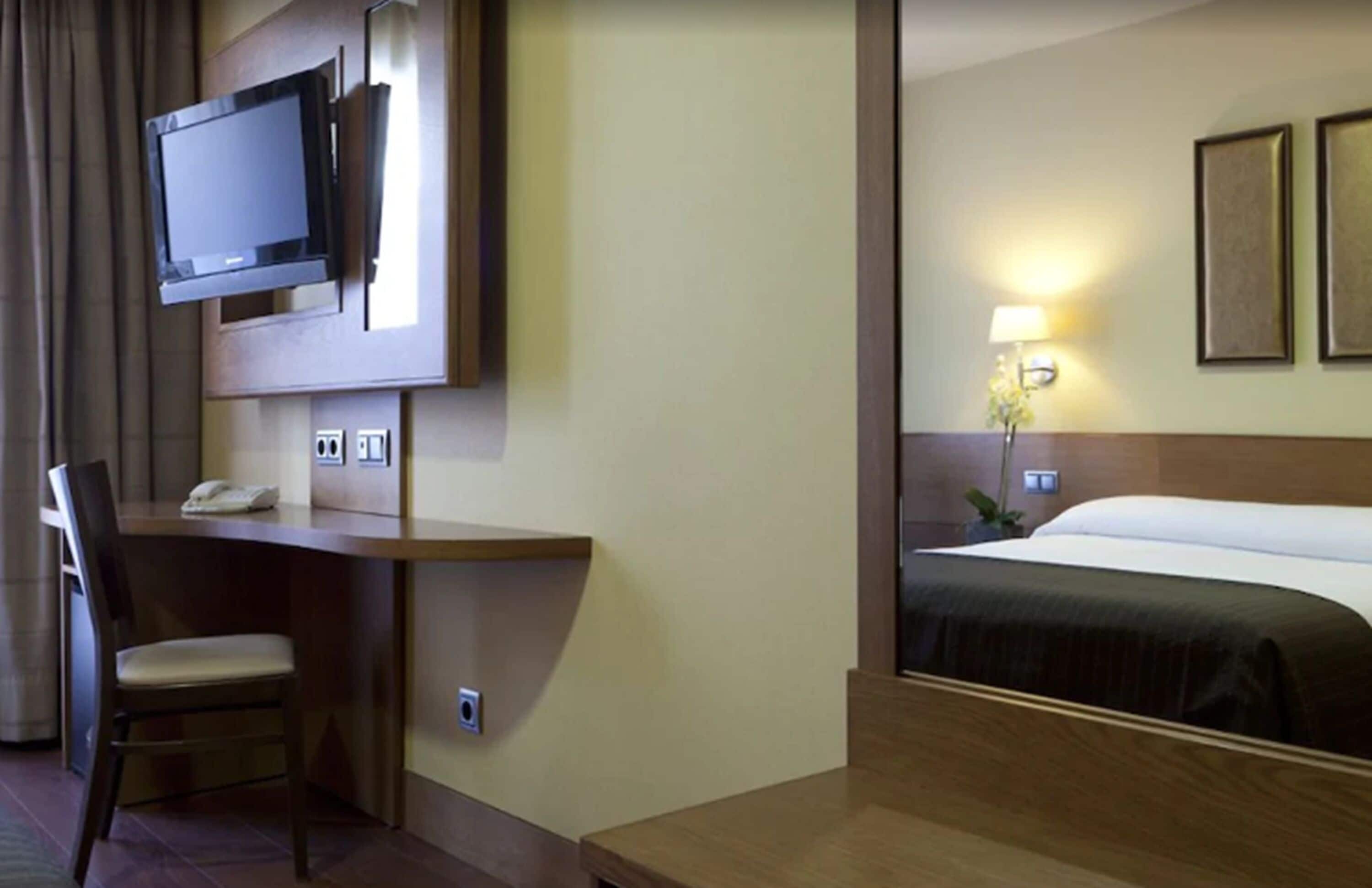 A hotel room with a bed, a desk with a chair, a television, and a lamp.