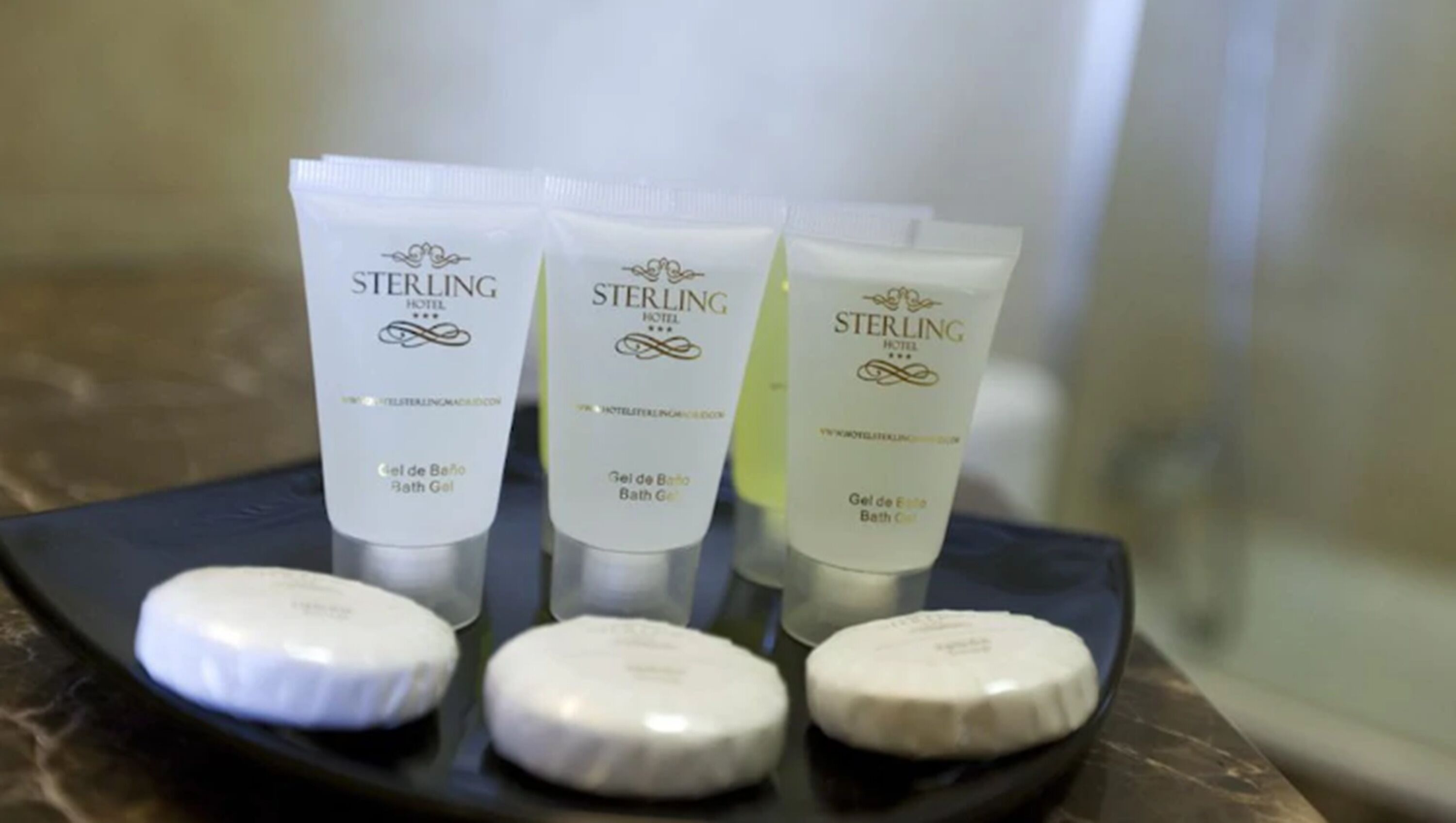 Three tubes of Sterling Hotel bath gel and three round soap bars on a tray.