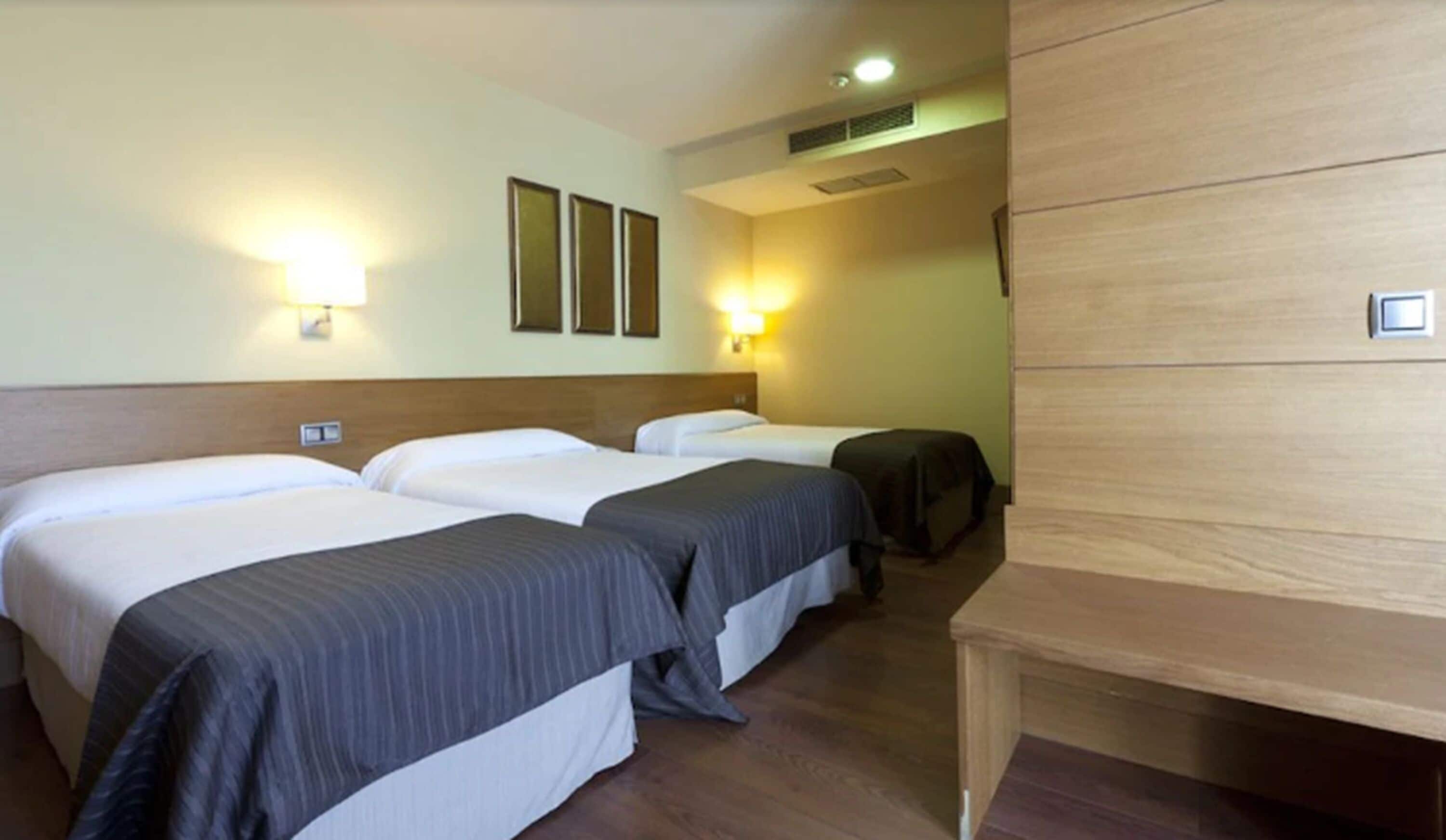 A hotel room with three single beds, a wooden headboard, and a small desk.