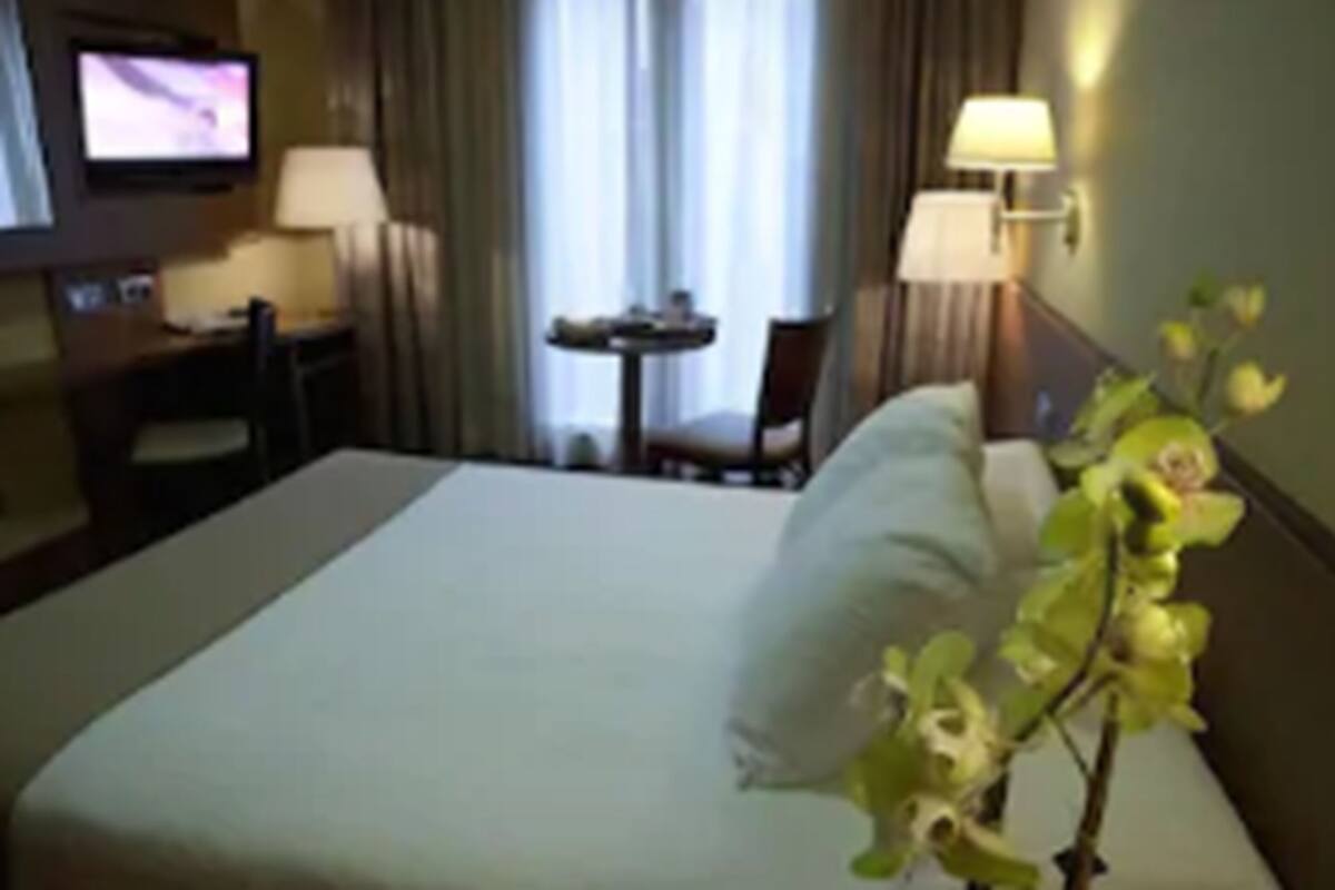 Una habitación de hotel con cama, escritorio, silla, televisor y lámpara.