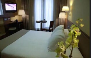 Ein Hotelzimmer mit Bett, Schreibtisch, Stuhl, Fernseher und Lampe.