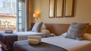 Ett hotellrum med två sängar, en sänggavel i trä, ett nattduksbord med en telefon och ett fönster med utsikt över byggnader.